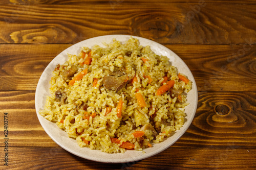 Pilaf with meat, rice, carrot and onion in a plate on wooden table