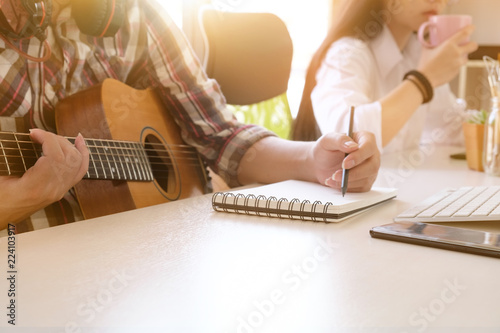 Fototapeta musician songwriter working with guitar and notepad paper on workplace with cropped shot
