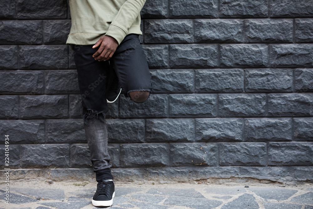 Male legs in torn jeans against brick wall background
