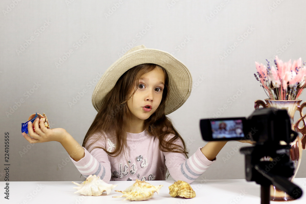 beautiful baby blogger in a hat talks about vacation, on the table and in the hands of a seashell beautiful baby blogger in a hat talks about vacation, on the table and in the hands of a seashell