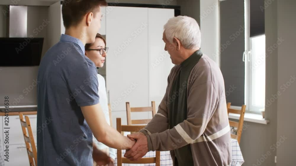 Medium shot of two volunteers hugging and shaking hands with elderly man and talking to him when visiting him at home Medium shot of two volunteers hugging and shaking hands with elderly man and talking to him when visiting him at home