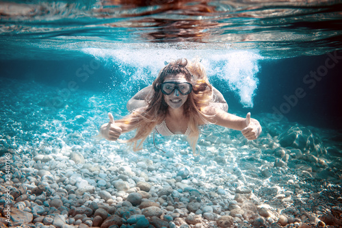 Snorkeling in the tropical sea, woman shows thumb up sign underwater