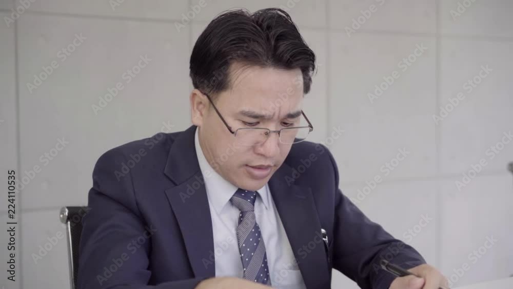 Slow motion - Businessman upset at desk in office. Asian businessman being depressed by working in office. Yong business man to think and not Work with stress Pretending to put his hand to the head. Slow motion - Businessman upset at desk in office. Asian businessman being depressed by working in office. Yong business man to think and not Work with stress Pretending to put his hand to the head.