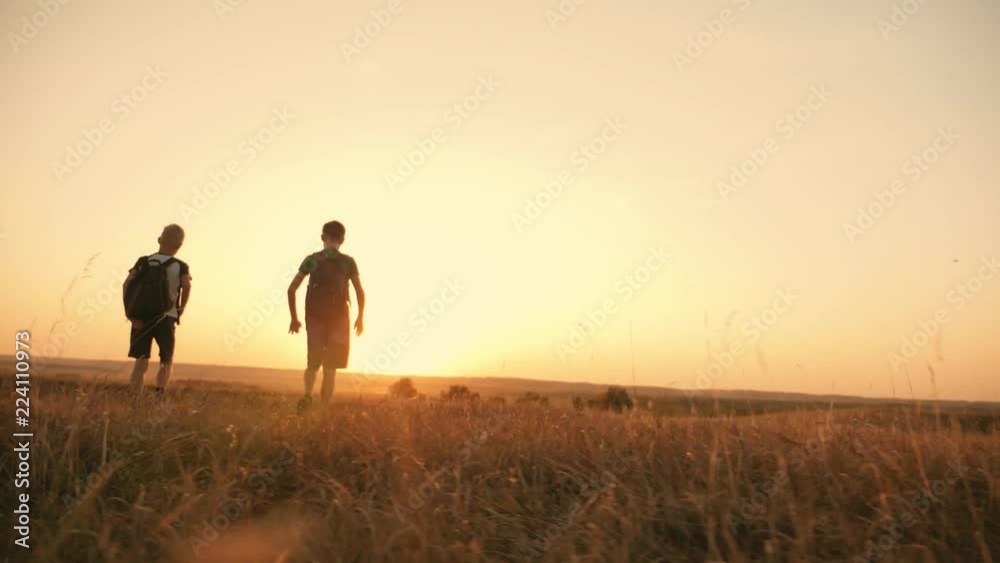 Two travelers boy. Two boys are walking along the field at sunset with rucksacks. The concept of family and travel Two travelers boy. Two boys are walking along the field at sunset with rucksacks. The concept of family and travel