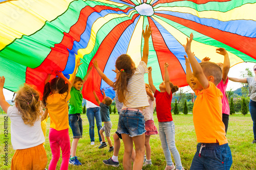 Joyous classmates jumping under colorful parachute in the summer outdoors
