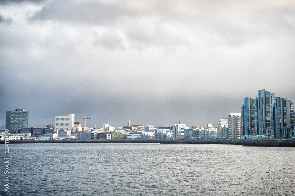 Reykjavik seascape dramatic cloudy sky. City on sea coast Iceland. Scandinavian seascape concept. Calm water surface and city with high buildings modern architecture. Scandinavian city at seashore