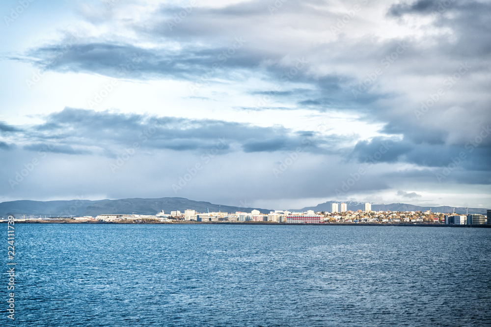 City on sea coast Iceland. Scandinavian seascape concept. Calm water surface and city with high buildings modern architecture. Scandinavian city at seashore. Reykjavik seascape dramatic cloudy sky