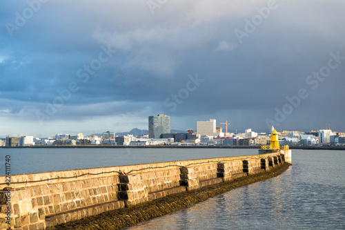 Lighthouse on sea pier in reykjavik iceland. Lighthouse yellow bright tower at sea shore. Seascape and skyline with bright lighthouse. Sea port navigation concept. Sea transportation and navigation © be free