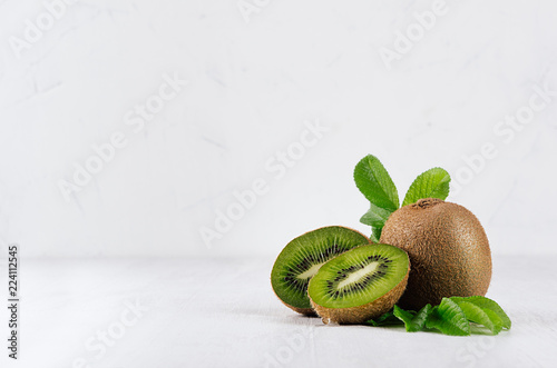 Ripe green kiwi with half cut and juice drop flow down and young leaves on white wood board as fresh summer fruits background.