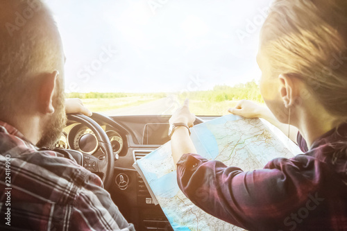 rear view of a cute couple sitting in a car with a map going on the road