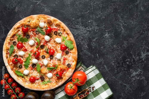 Tasty pizza on black concrete background, top view and copy space for text. Italian pizza with tomato, mozzarella cheese, black olives and arugula