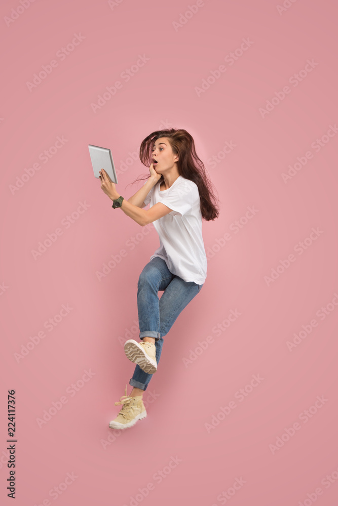 Gadget in modern life. Jump of young woman over pink studio background using laptop or tablet gadget while jumping. Runnin surprised girl in motion or movement. Human emotions and facial expressions Gadget in modern life. Jump of young woman over pink studio background using laptop or tablet gadget while jumping. Runnin surprised girl in motion or movement. Human emotions and facial expressions