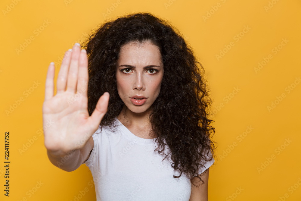 Image of confident woman 20s with curly hair doing stop gesture with hand, isolated over yellow background