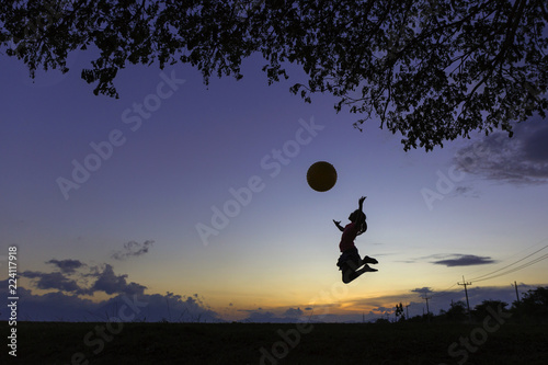 A schoolgirl juming with big ball under the tree in sunset.