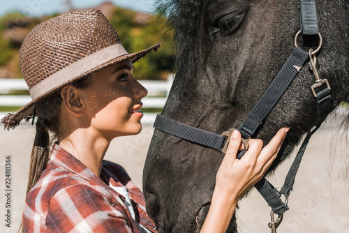 portrait of attractive female equestrian touching and looking at horse at ranch