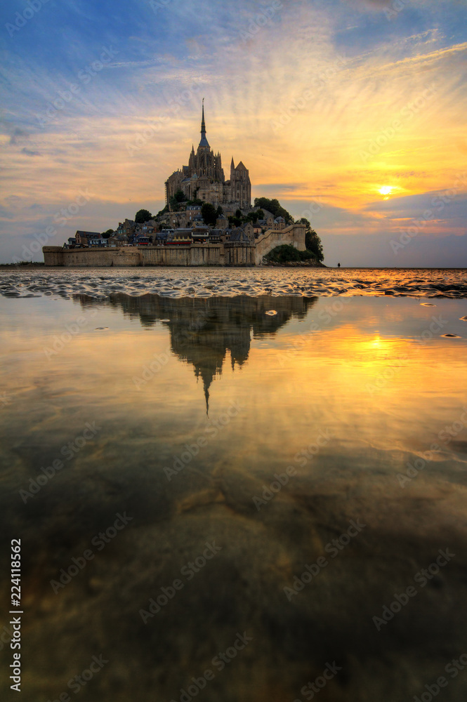 Fototapeta premium Beautiful view of historic landmark Le Mont Saint-Michel in Normandy, France, a famous UNESCO world heritage site and tourist attraction, at sunset with reflection