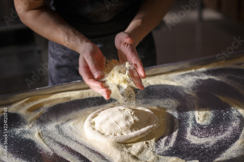 Photos Baker sprinkles dough for pizza by semolina