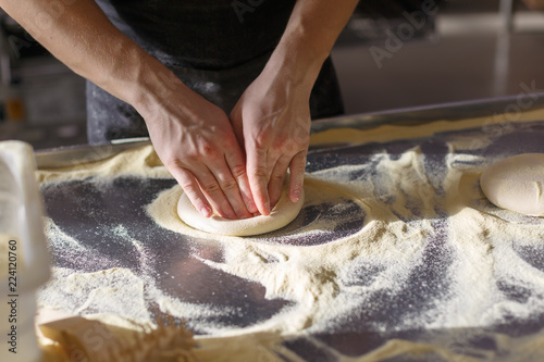 Baker kneads dough for pizza in the kitchen in the restaurant