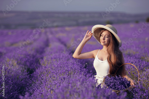 Beautiful young teen girl outdoors portrait. Brunette in hat with basket flowers harvesting in lavender field Provence, at sunset. Attractive pretty girl with long healthy curly hair.