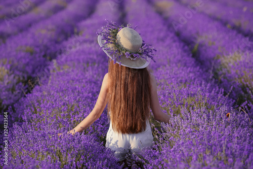 Beautiful healthy long hair. Back view of Young teen girl in hat over lavender field. Happy carefree woman with shiny hairstyle enjoying sunset. Outdoors portrait. Provence, France.