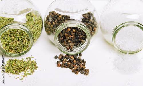 Popular spices in small jars scattered on white background. Sea salt  pepper and spicy herbs.