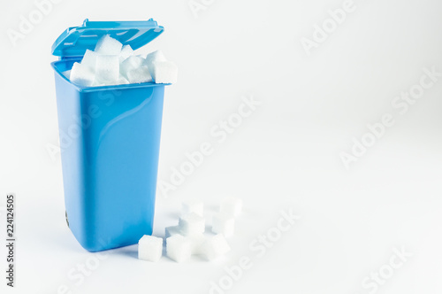 Blue trash can full of sugar cubes, white background