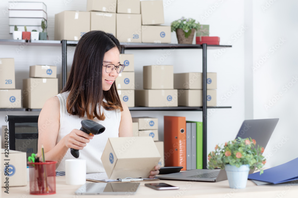 Young and beautiful Asian woman using bar code machine with smiling face happy check orders online customers in the homeoffice. Concept for home base business and startup ownership.