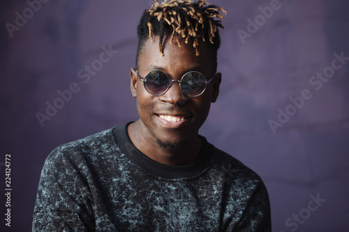 Stylish smile african american man rapper with dreadlocks at violet wall background