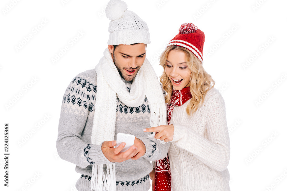 beautiful smiling young couple in sweaters, scarves and hats using smartphone isolated on white beautiful smiling young couple in sweaters, scarves and hats using smartphone isolated on white