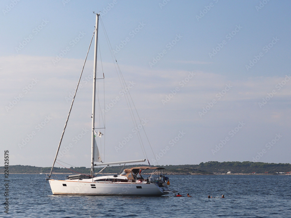 A modern sailing yacht is anchored in a bay. People bathe in the sea. Active rest on the Adriatic Sea of the Mediterranean region. Dalmatian riviera of Croatia. Prestigious and rich lifestyle A modern sailing yacht is anchored in a bay. People bathe in the sea. Active rest on the Adriatic Sea of the Mediterranean region. Dalmatian riviera of Croatia. Prestigious and rich lifestyle