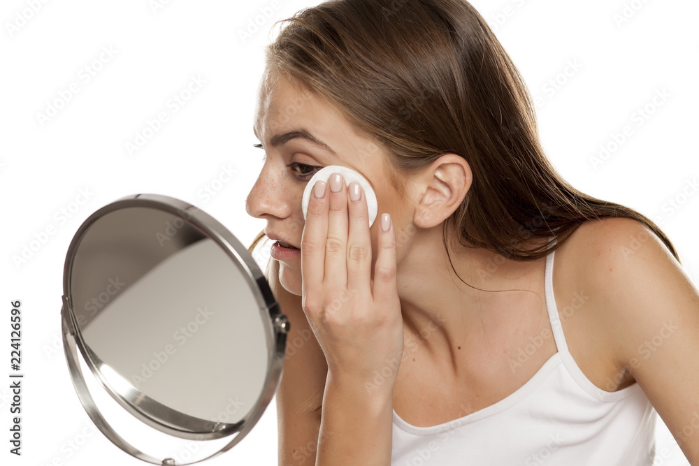 young beautiful girl cleaning her face with cotton pads on white backgeound young beautiful girl cleaning her face with cotton pads on white backgeound