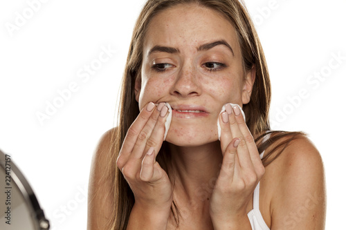 young beautiful girl cleaning her face with cotton pads on white backgeound photo
