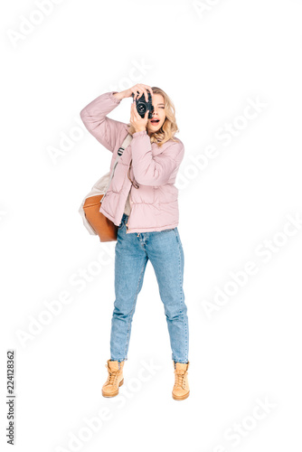 full length view of young woman with backpack photographing with camera isolated on white © LIGHTFIELD STUDIOS