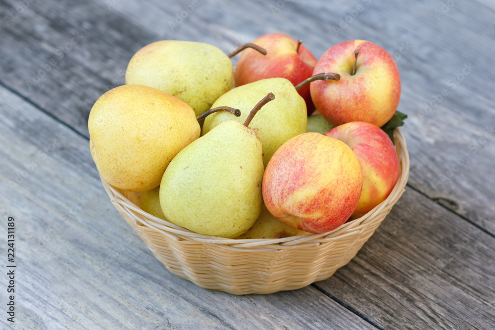 Fresh apples and pears in wicker plate on wooden background in rural style