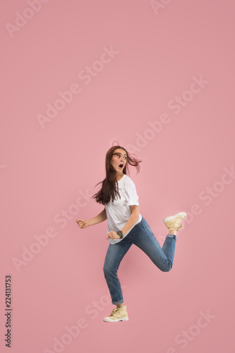 Freedom in moving. Mid-air shot of pretty frightened running away young woman jumping against pink studio background. Runnin girl in motion or movement. Human emotions and facial expressions concept