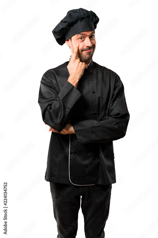 Chef man In black uniform standing and looking to the front opening the eye with finger on isolated white background Chef man In black uniform standing and looking to the front opening the eye with finger on isolated white background