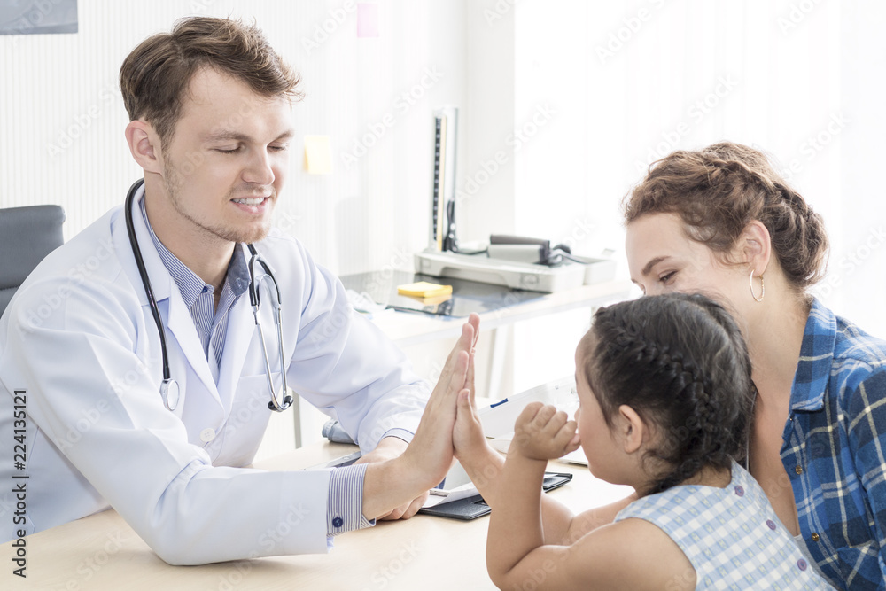 Obraz premium Pediatrician (doctor) man giving fist bump (High Five To),reassuring and discussing kid at surgery.Mother Caucasian and kid smiling in hospital room.Copy space.