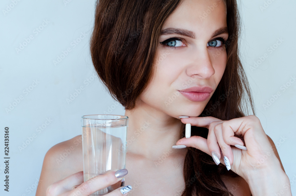 Naklejka premium portrait of a beautiful woman holding a big pill and a glass of water. concept vitamins for hair, skin and nails