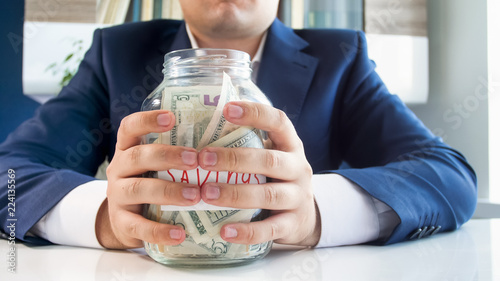 Tableau sur toile Closeup photo of young greedy businesman holding glass jar full of money in hand