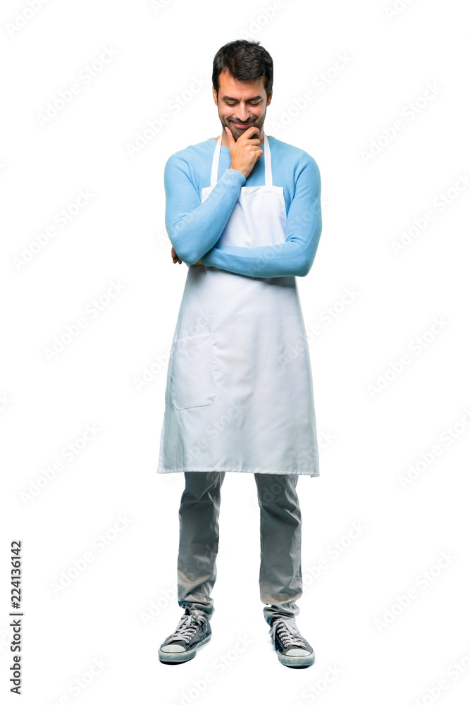 A full-length shot of a Man wearing an apron standing and looking down with the hand on the chin on isolated background A full-length shot of a Man wearing an apron standing and looking down with the hand on the chin on isolated background