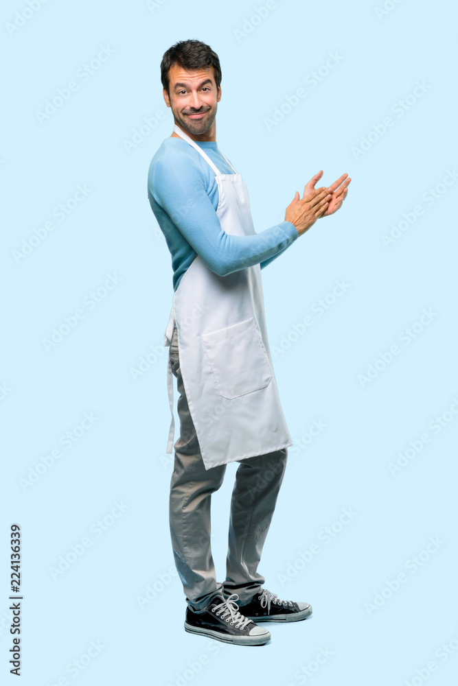 Full body of Man wearing an apron applauding after presentation in a conference on blue background Full body of Man wearing an apron applauding after presentation in a conference on blue background