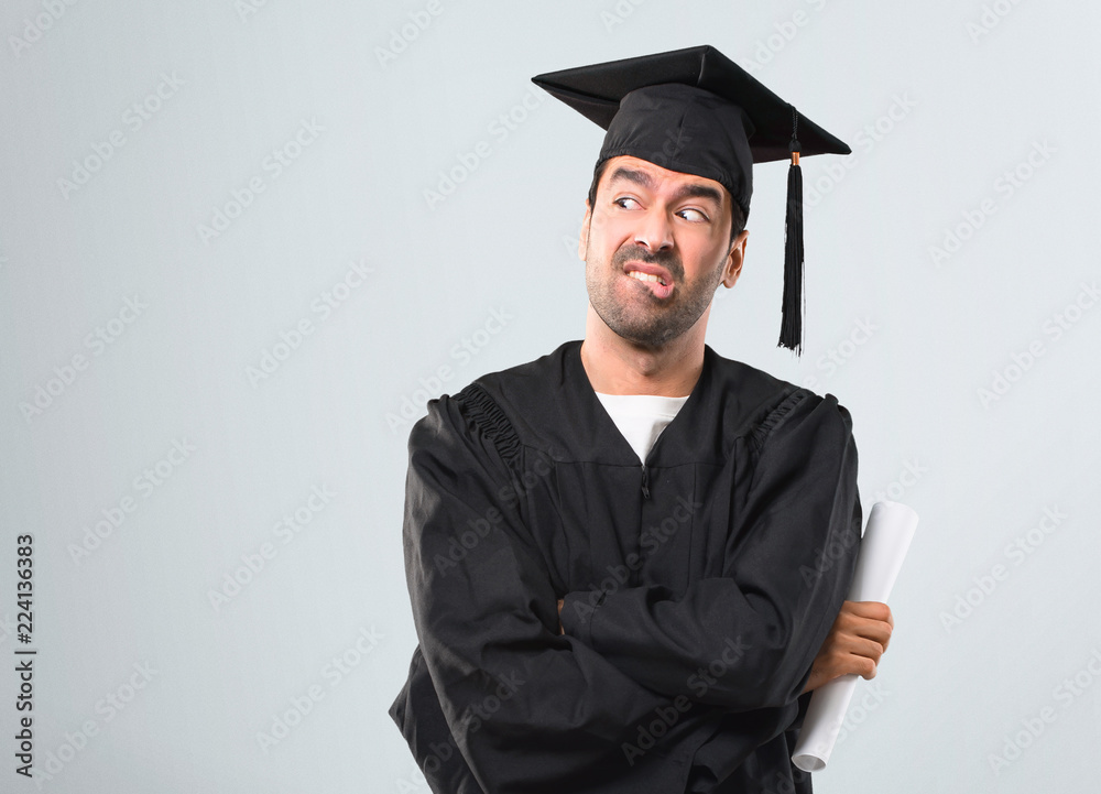 Man on his graduation day University having doubts and with confuse face expression while bites lip. Questioning an idea on grey background Man on his graduation day University having doubts and with confuse face expression while bites lip. Questioning an idea on grey background
