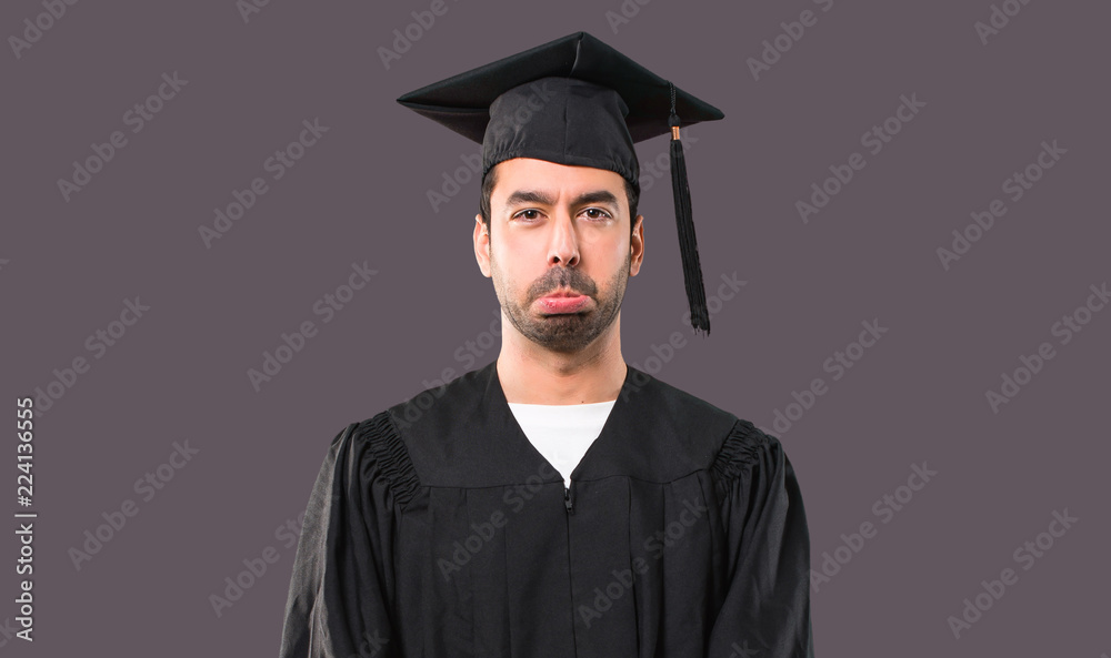 Man on his graduation day University with sad and depressed expression. Serious gesture on violet background Man on his graduation day University with sad and depressed expression. Serious gesture on violet background