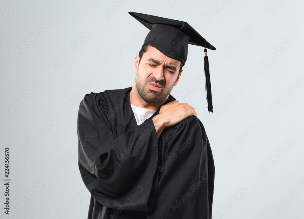 Man on his graduation day University suffering from pain in shoulder for having made an effort on grey background