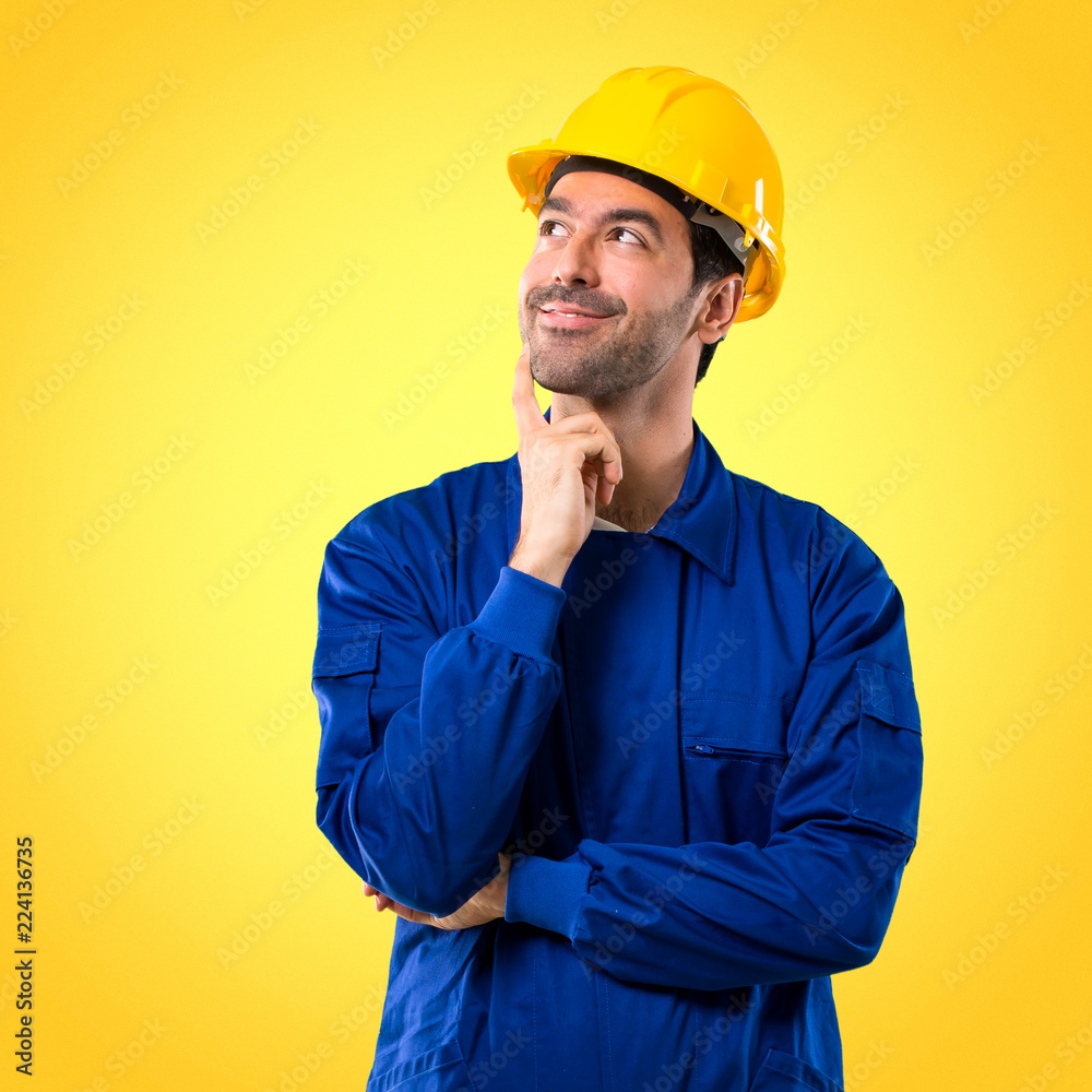 Young workman with helmet standing and thinking an idea while looking up on yellow background Young workman with helmet standing and thinking an idea while looking up on yellow background