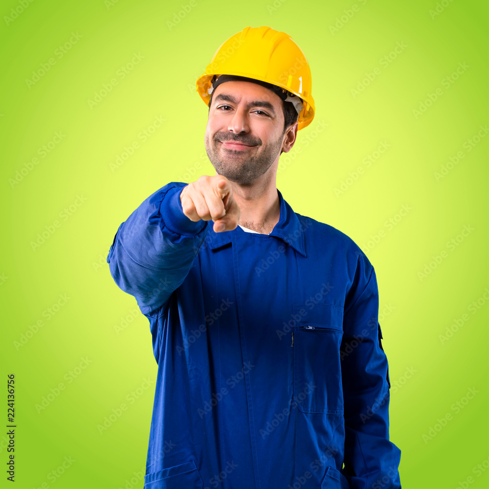 Young workman with helmet points finger at you with a confident expression on green background