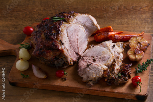 Baked ham with vegetables: carrots, onions, tomatoes, garlic and herbs on chopping board