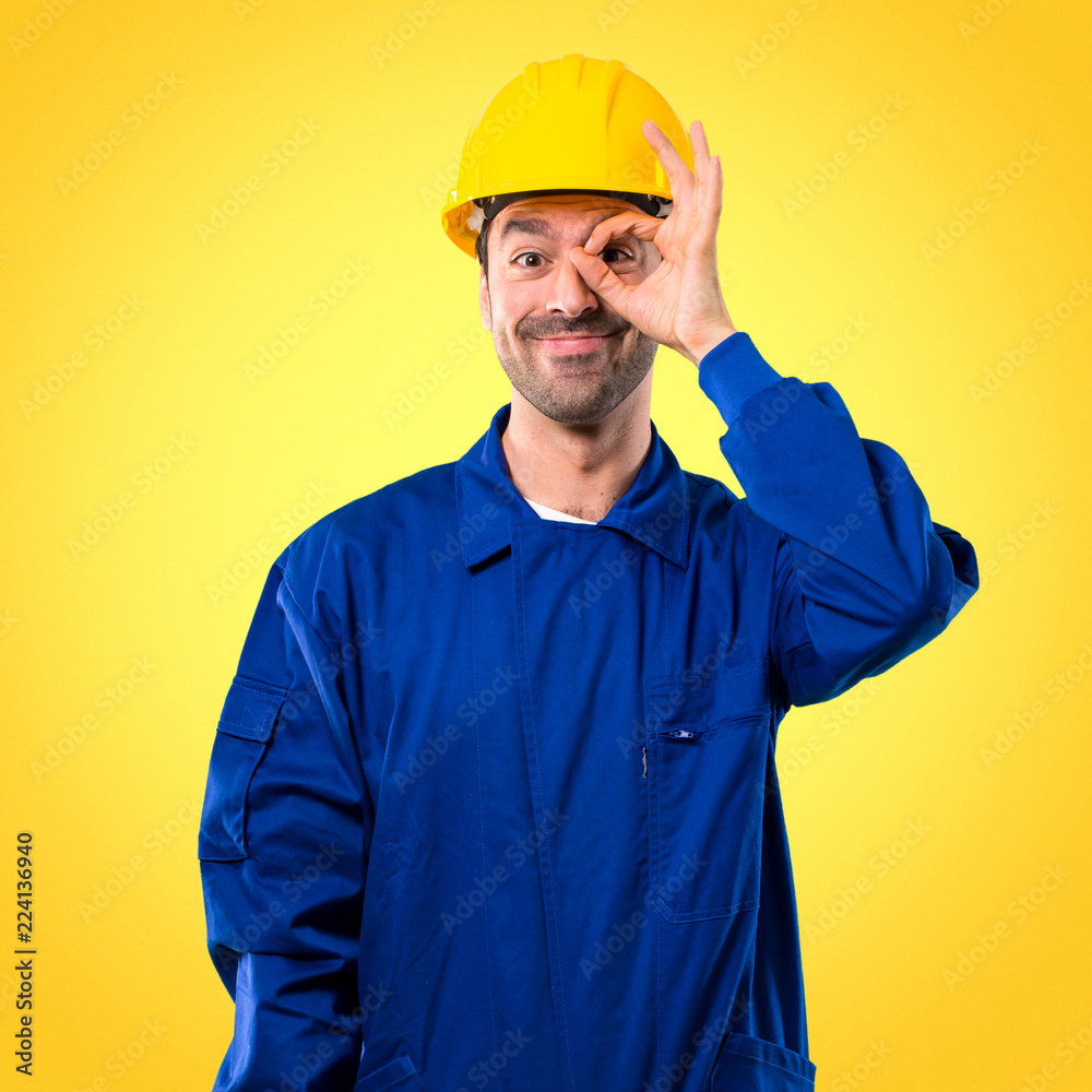 Young workman with helmet makes funny and crazy face emotion on yellow background Young workman with helmet makes funny and crazy face emotion on yellow background