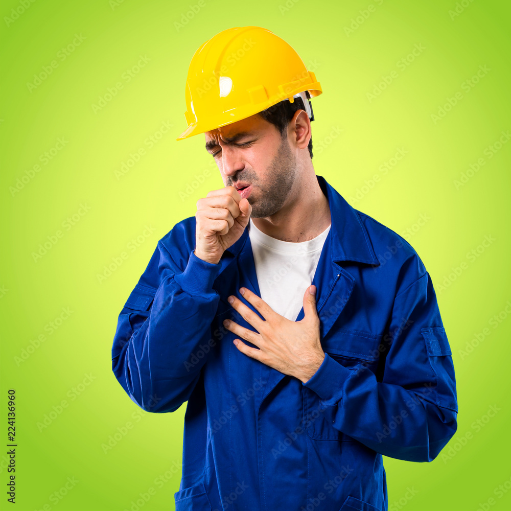 Young workman with helmet is suffering with cough and feeling bad on green background