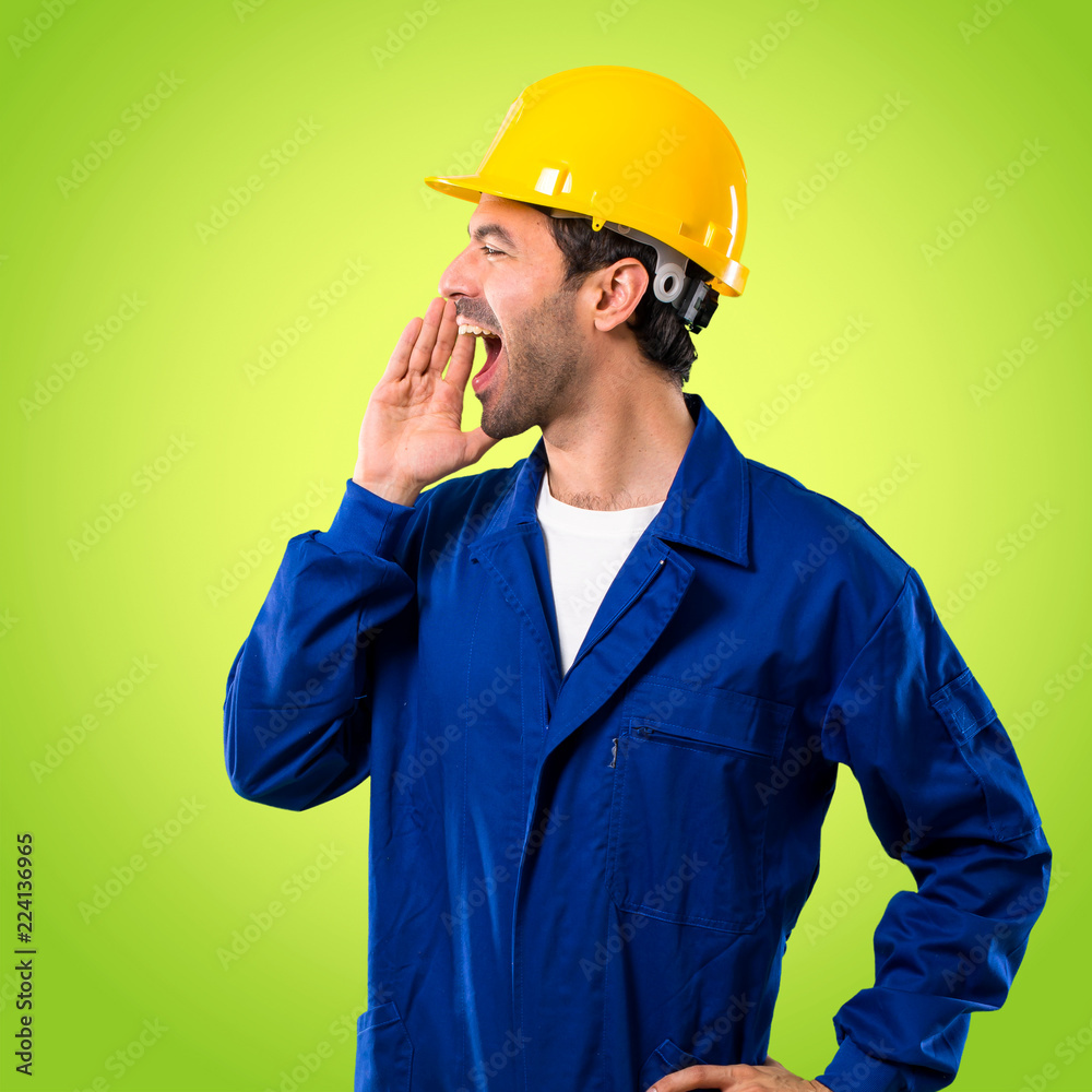 Young workman with helmet shouting with mouth wide open to the lateral and announcing something on green background Young workman with helmet shouting with mouth wide open to the lateral and announcing something on green background